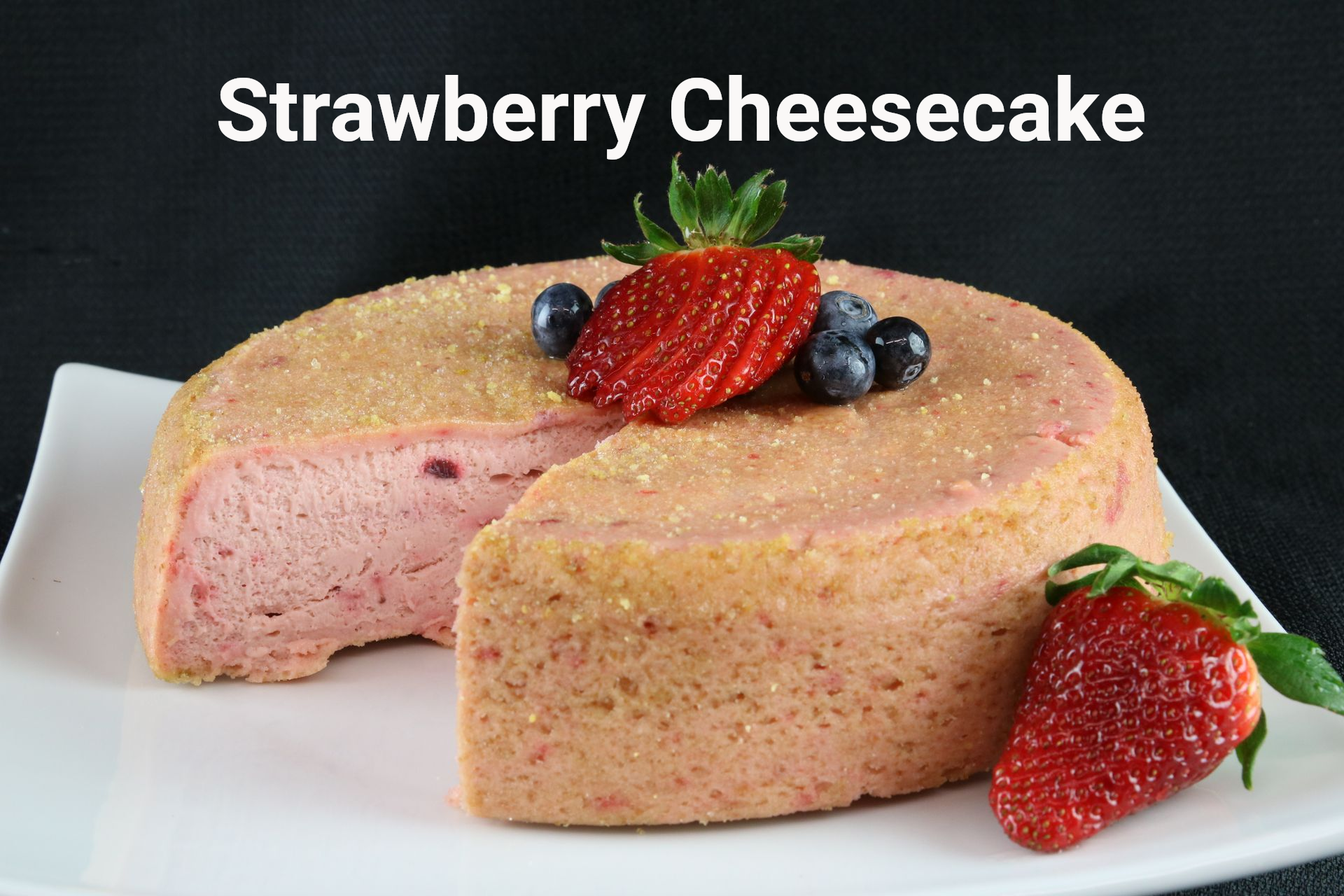 Strawberry cheesecake on a white plate, topped with strawberries and blueberries.