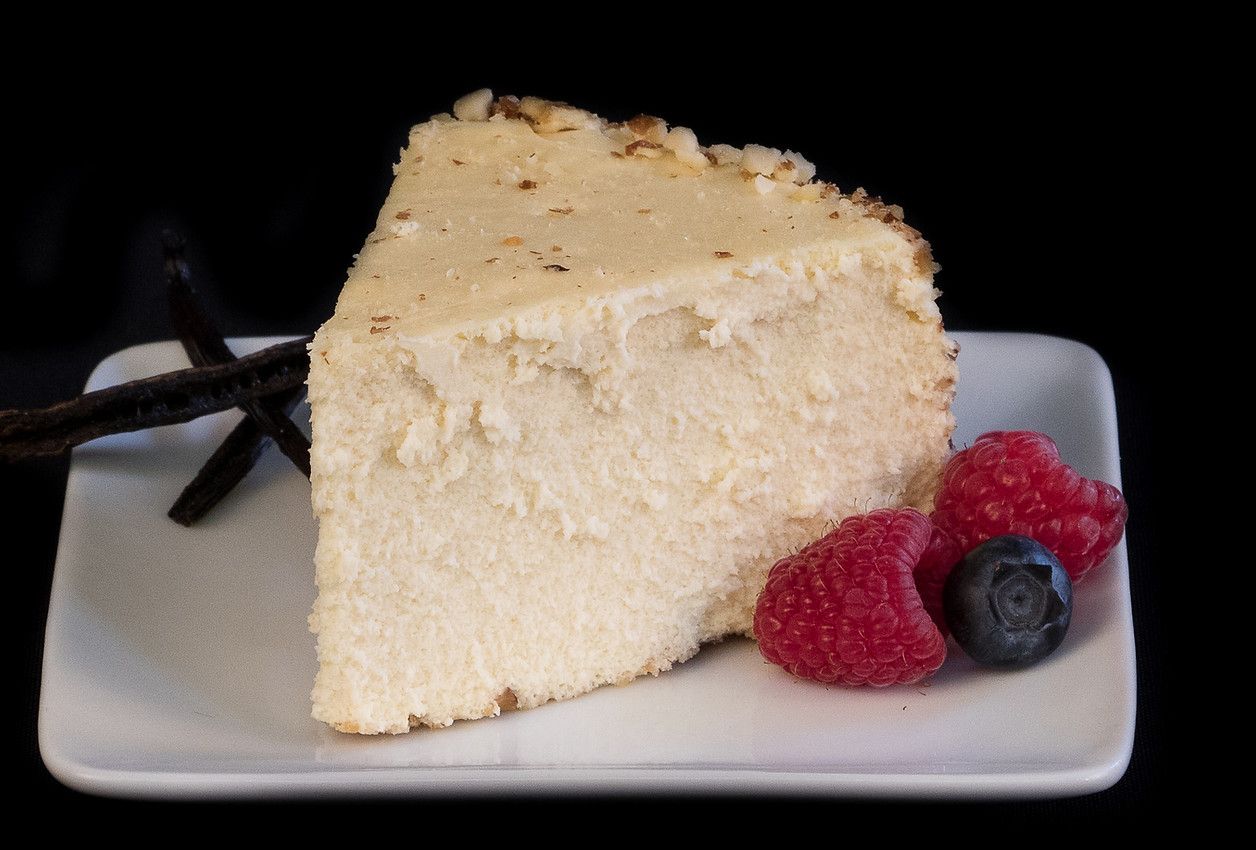 A slice of cheesecake with raspberries and blueberries on a white plate.