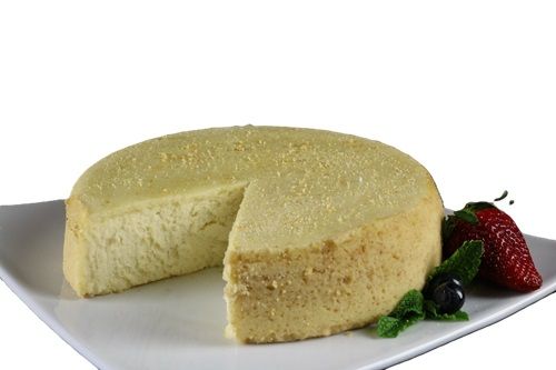A cheesecake with a slice taken out of it is on a white plate with strawberries and blueberries.