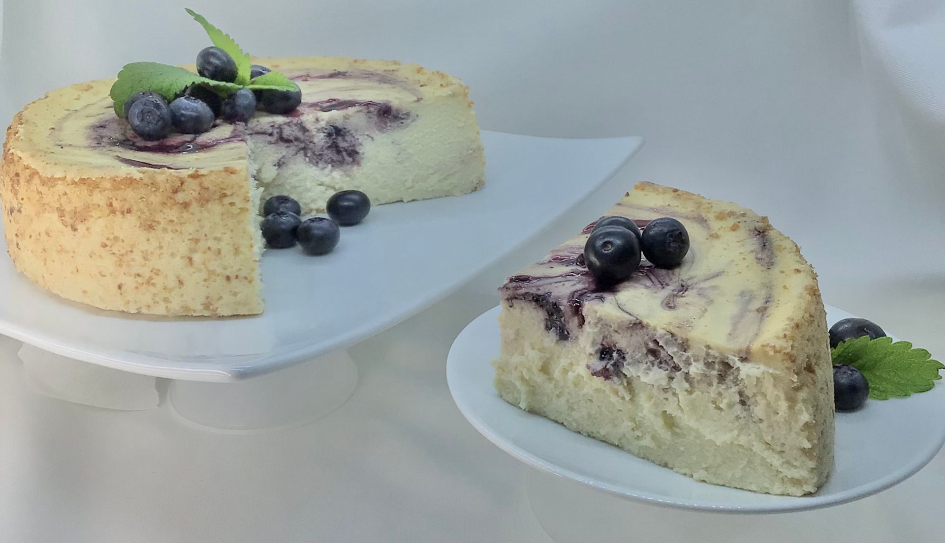 A slice of blueberry cheesecake is on a plate next to a whole cheesecake.