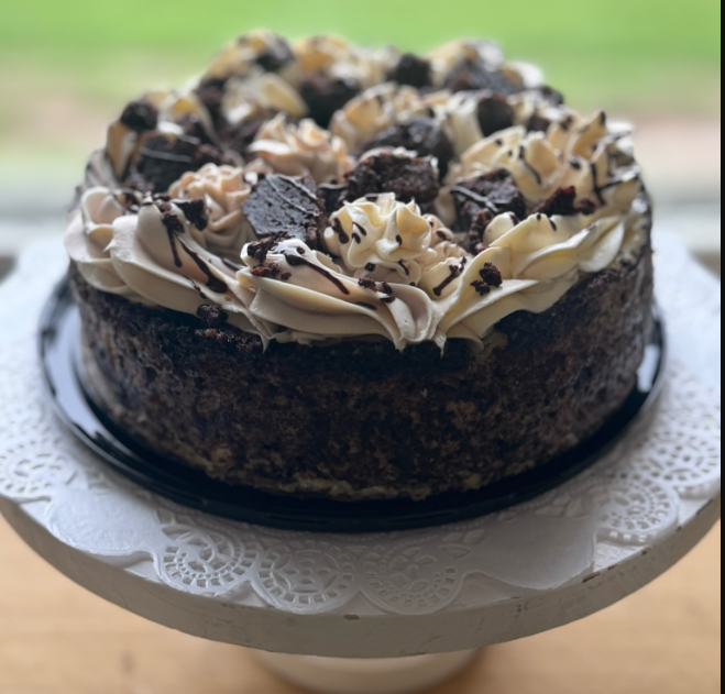 Chocolate cake with creamy frosting and chocolate pieces on a white cake stand.