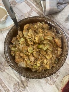 A brown bowl of stuffing with celery, onions, and seasonings, on a patterned tablecloth.