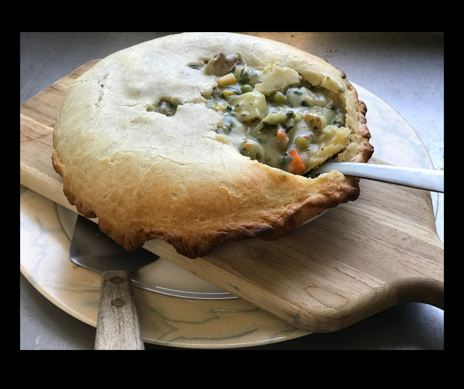 Pot pie on a wooden board, crust is golden brown and a spoon is scooping filling.