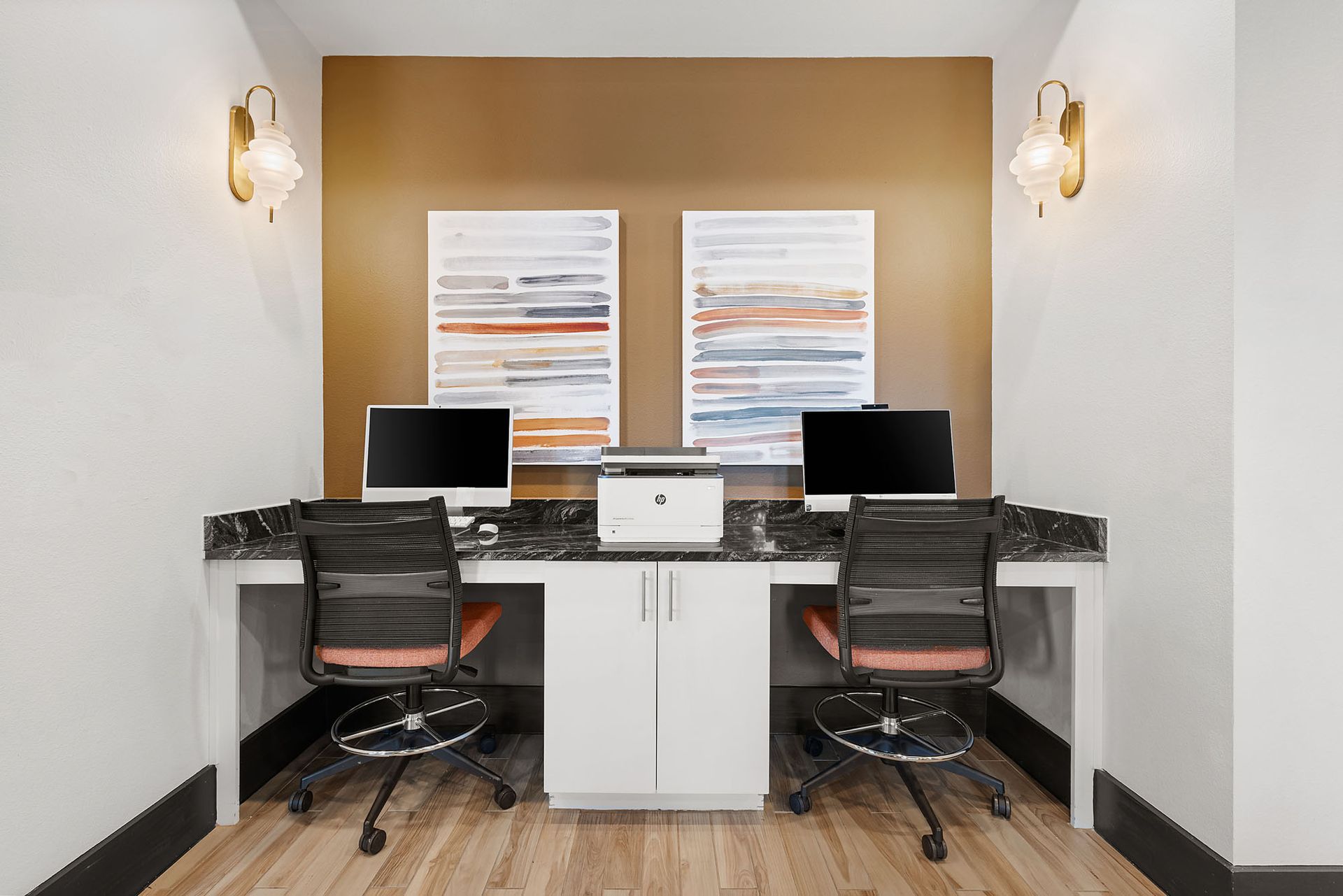 Modern home office with dual desks, black chairs, and two computers against a tan accent wall at Two99 Monroe.