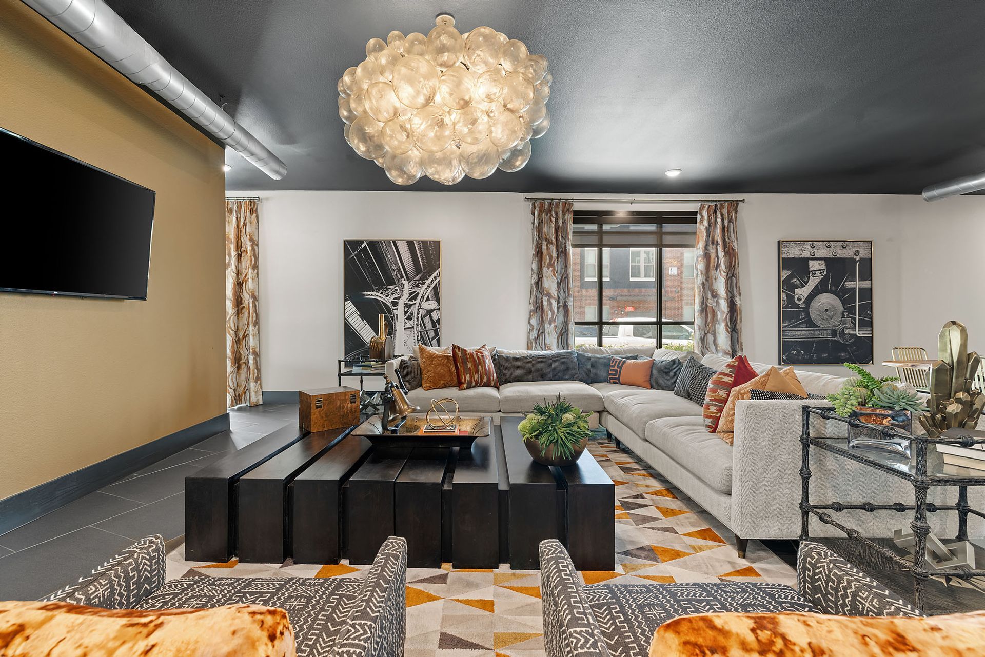 Modern living room with a sectional sofa, black coffee table, chandelier, and abstract wall art at Two99 Monroe.