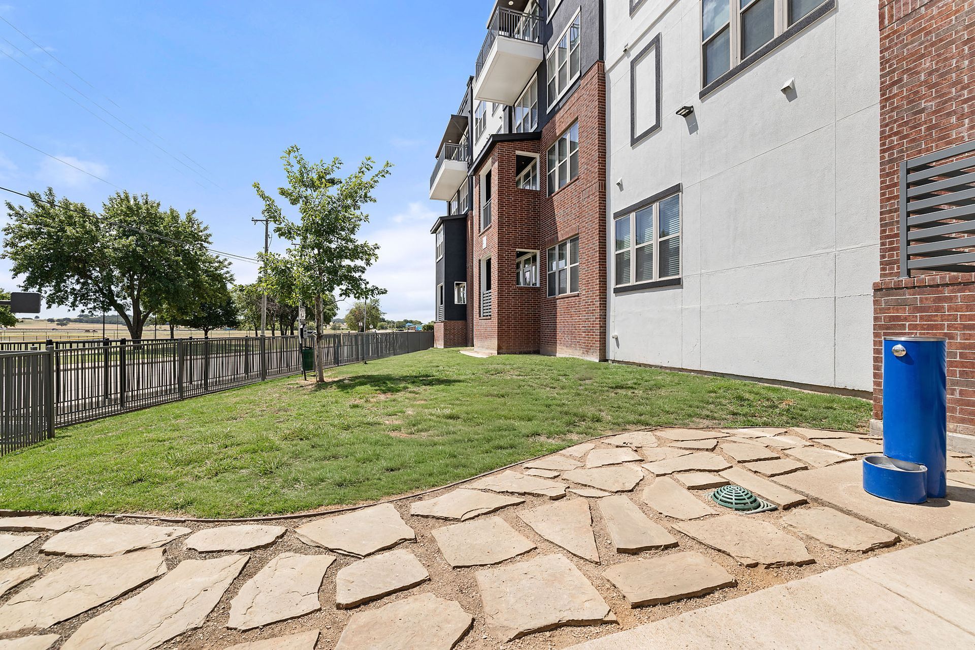 Apartment building exterior with grassy courtyard, stone path, and blue utility post at Two99 Monroe.