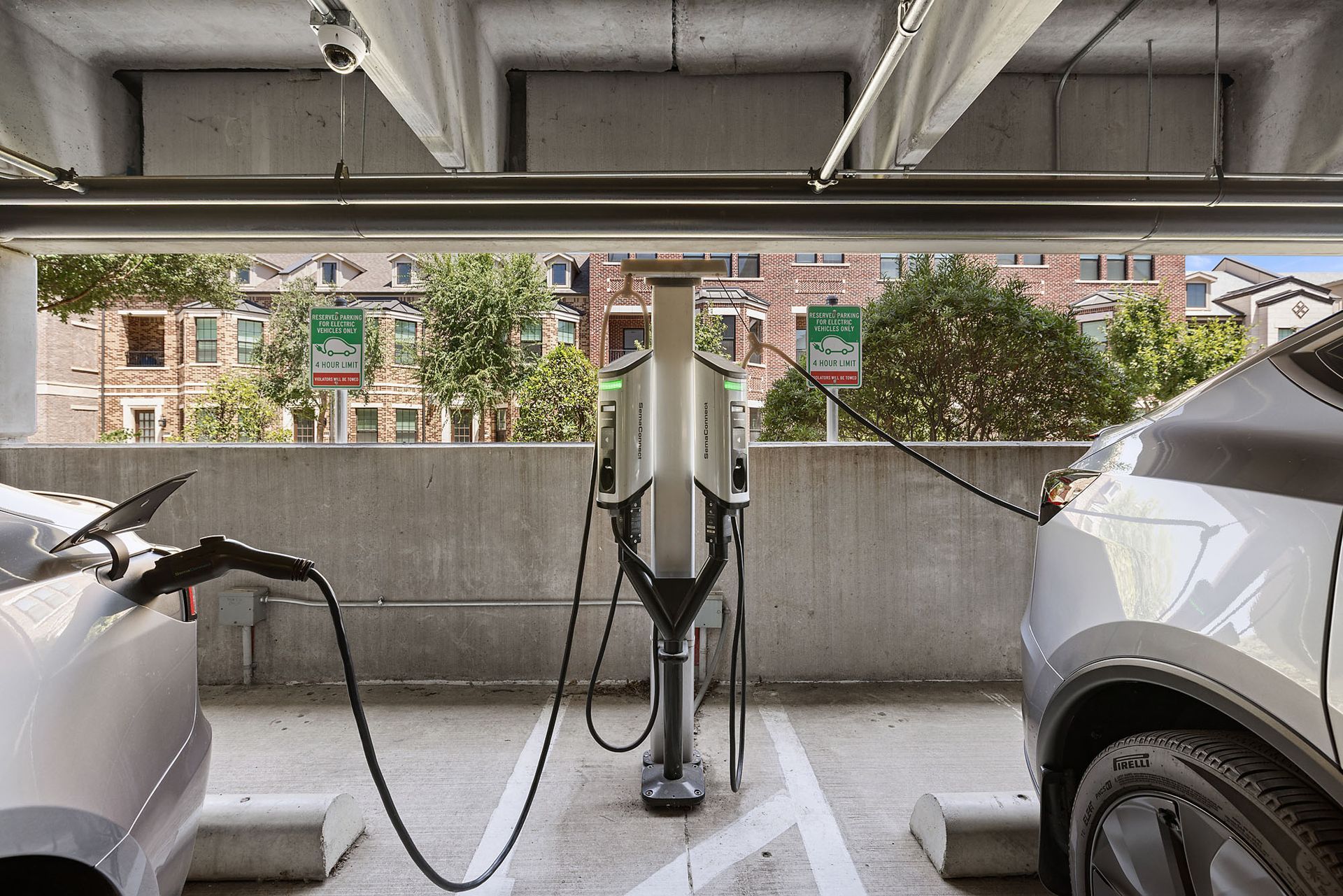 Electric car plugged into a charging station in a covered parking garage, with another car nearby at Two99 Monroe.