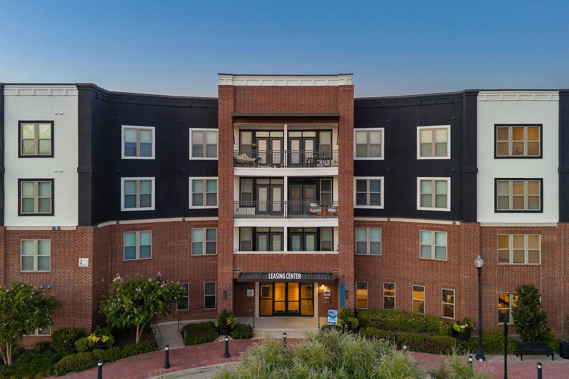 Apartment building facade with red brick center, dark gray sides, and lit entrance at Two99 Monroe.