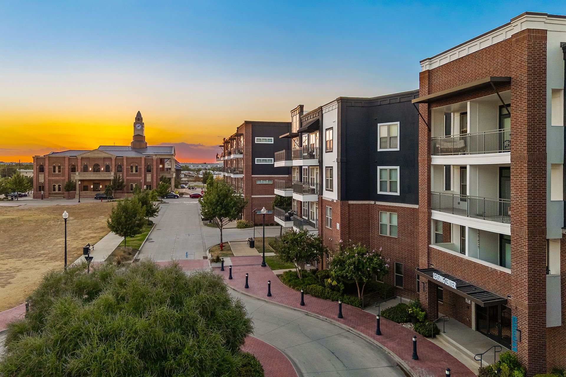 Apartment buildings at sunset beside a paved walkway and landscaped courtyard, with a distant clock tower at Two99 Monroe.