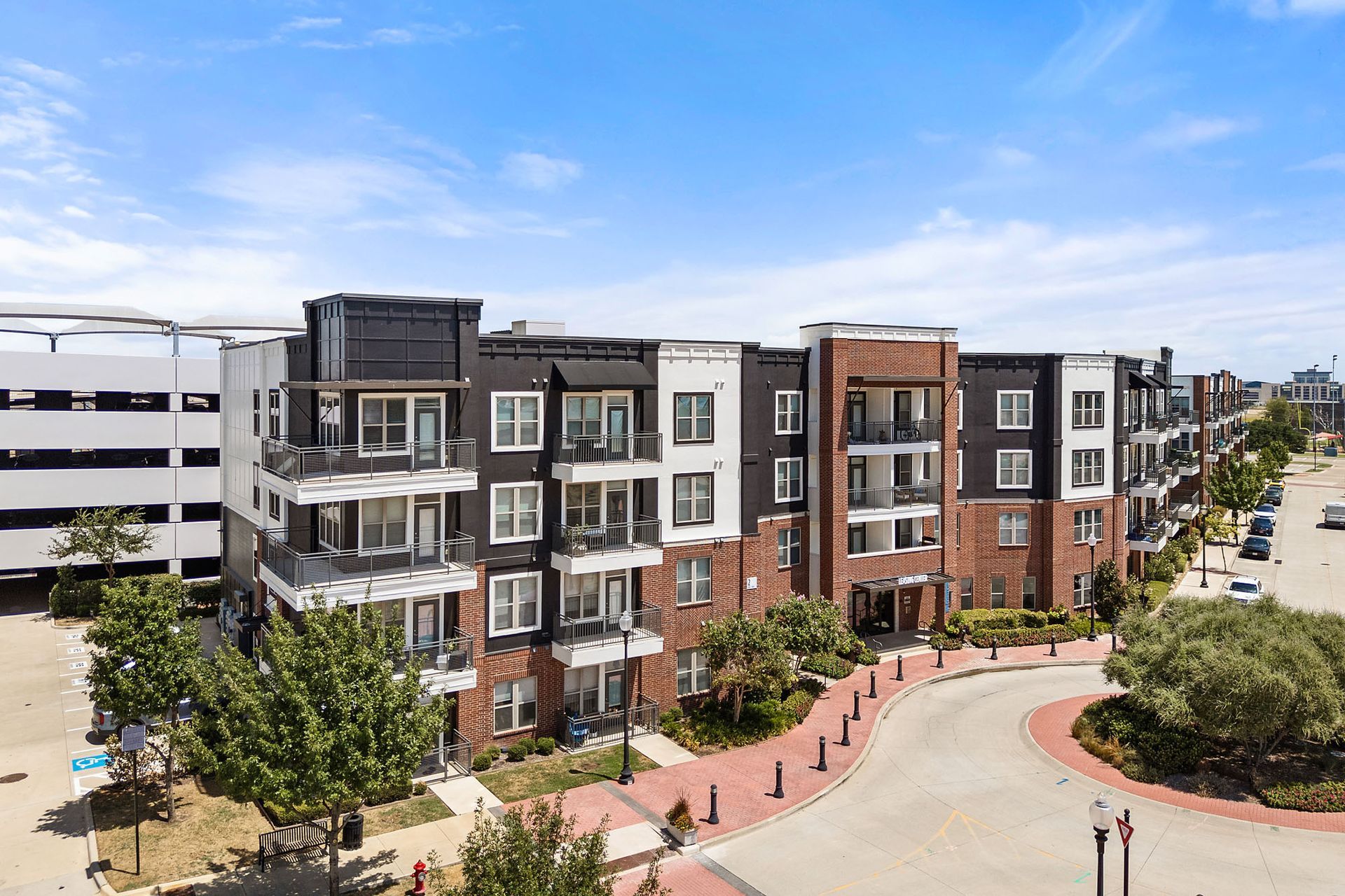 Modern apartment buildings along a landscaped street with a curved sidewalk and clear blue sky at Two99 Monroe.