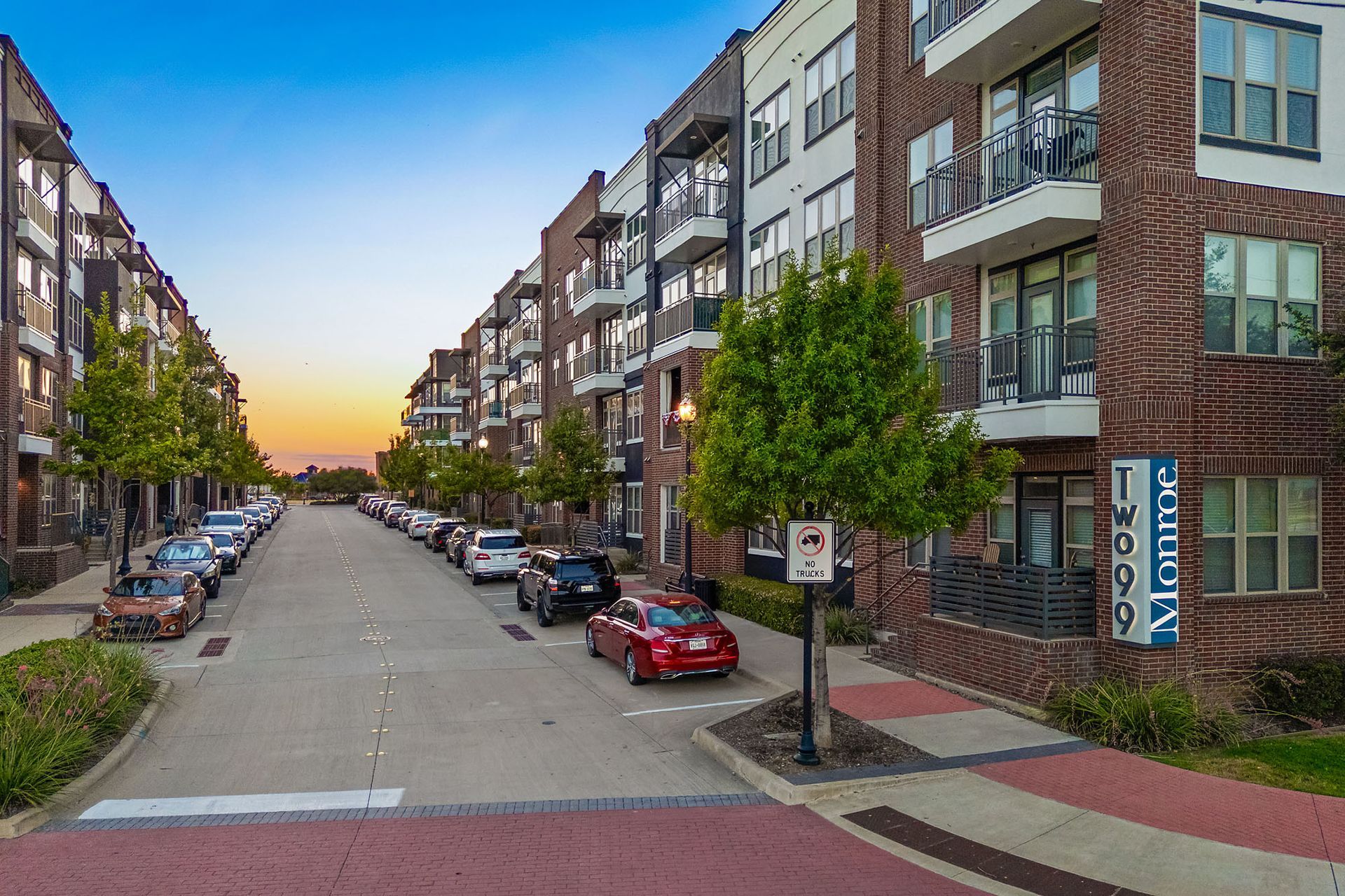 Quiet urban street with parked cars, apartment buildings, and a sunset sky at Two99 Monroe.