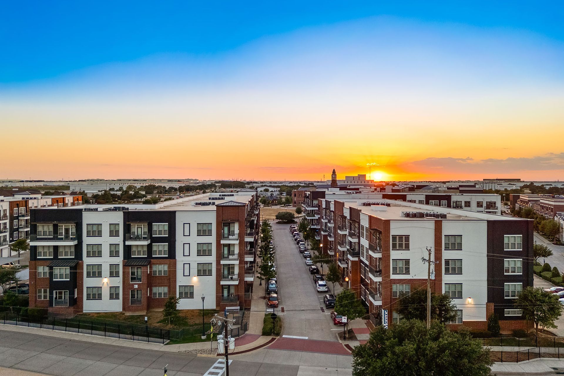 Sunset over a modern apartment complex with a street leading toward the horizon at Two99 Monroe.