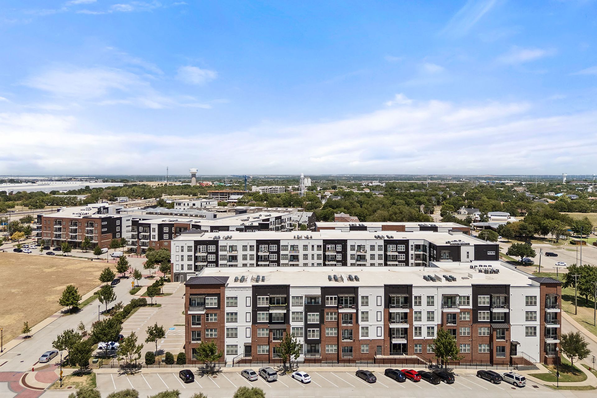 Aerial view of a modern apartment complex with parking lot under a blue sky at Two99 Monroe.