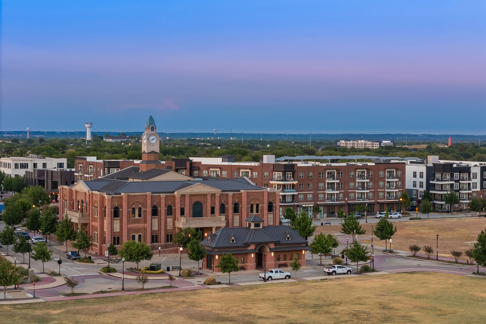 Aerial view of a brick campus building with a clock tower, surrounded by parking lots and trees at dusk at Two99 Monroe.
