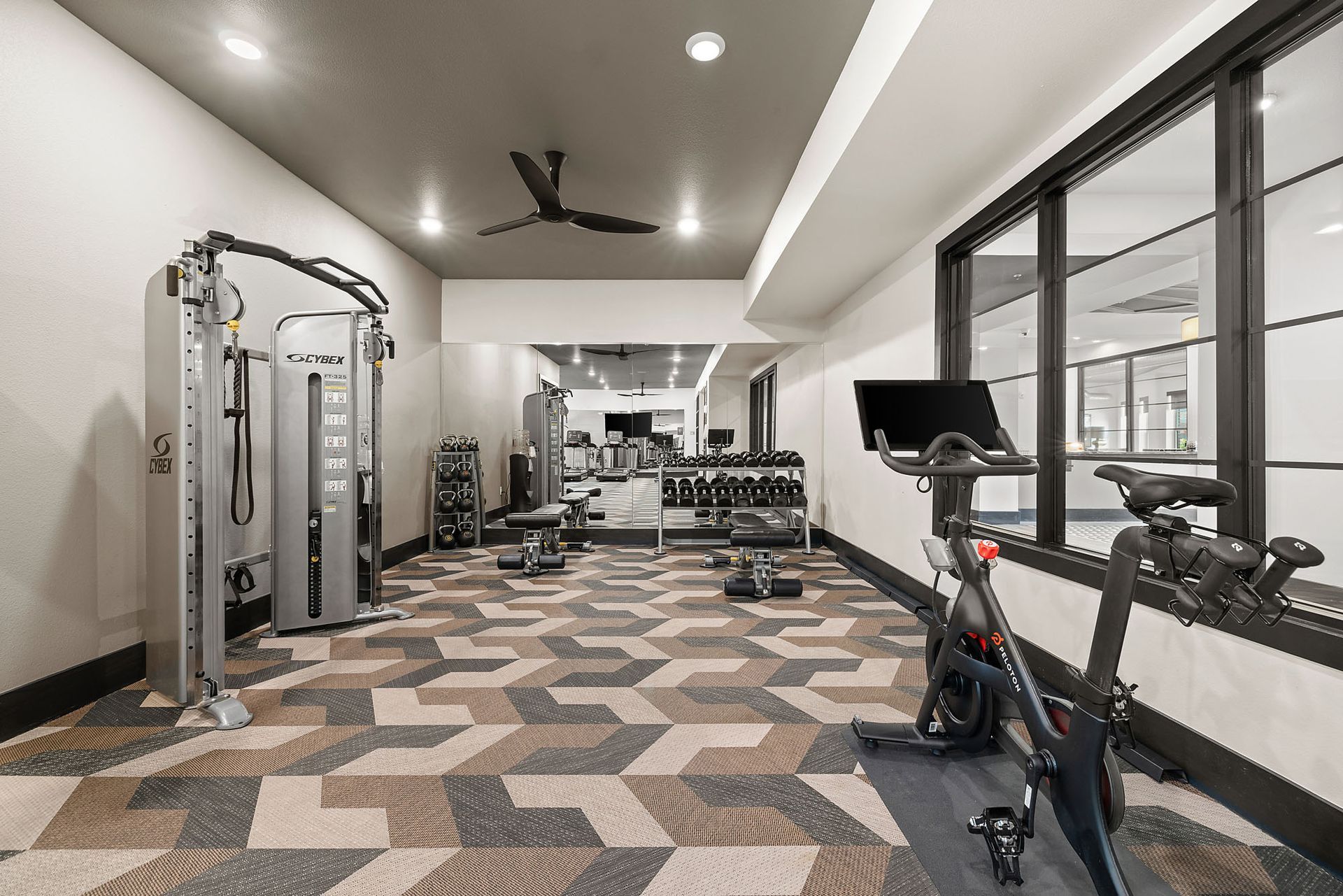 Modern gym with exercise machines, mirrored wall, large windows, and patterned carpet flooring at Two99 Monroe.