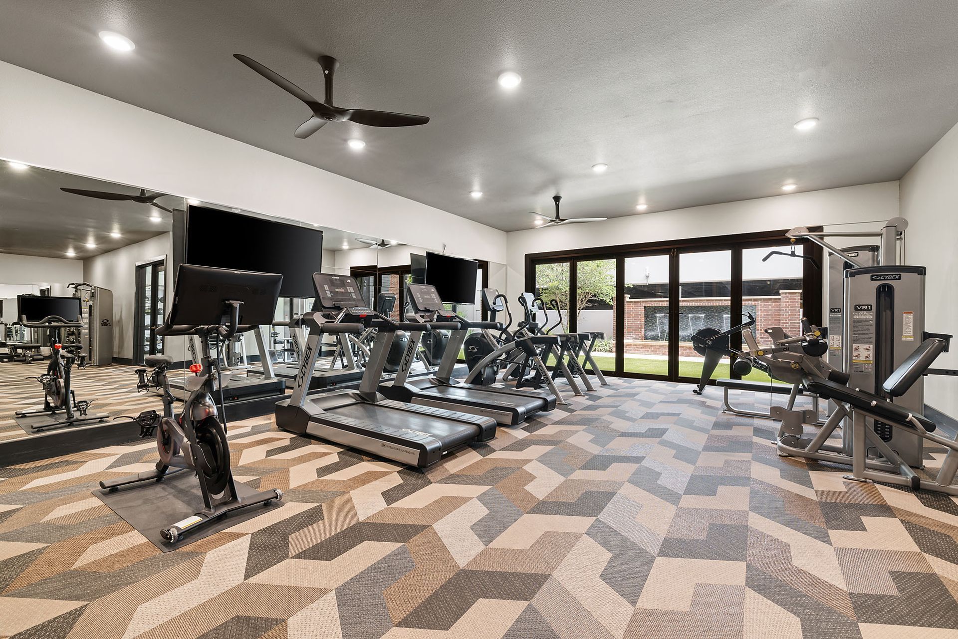 Modern gym with treadmills, exercise bikes, mirrors, and large windows overlooking greenery at Two99 Monroe.