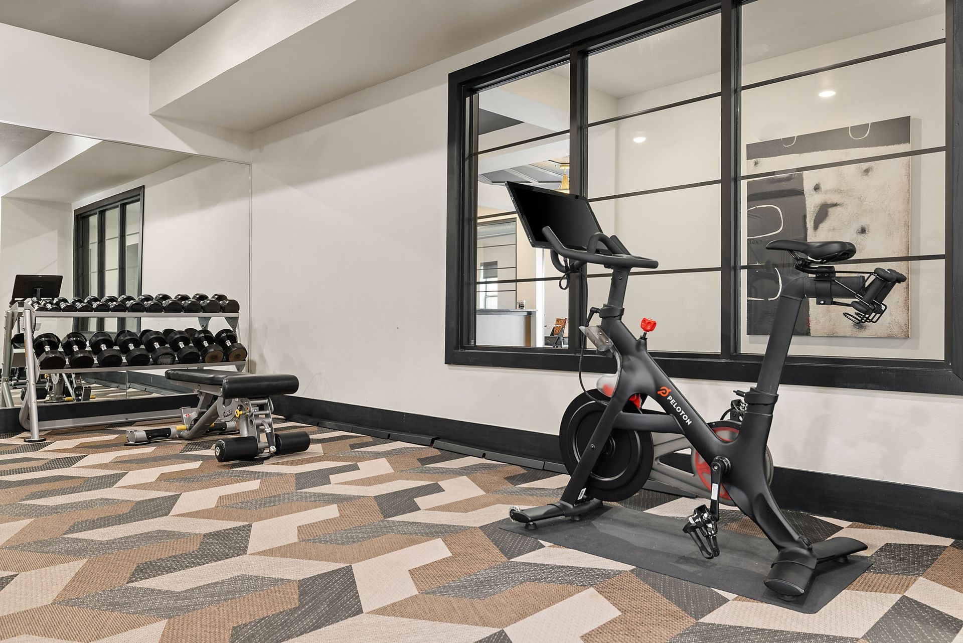 Gym with stationary bike, dumbbell rack, and wall mirror on patterned carpet at Two99 Monroe.