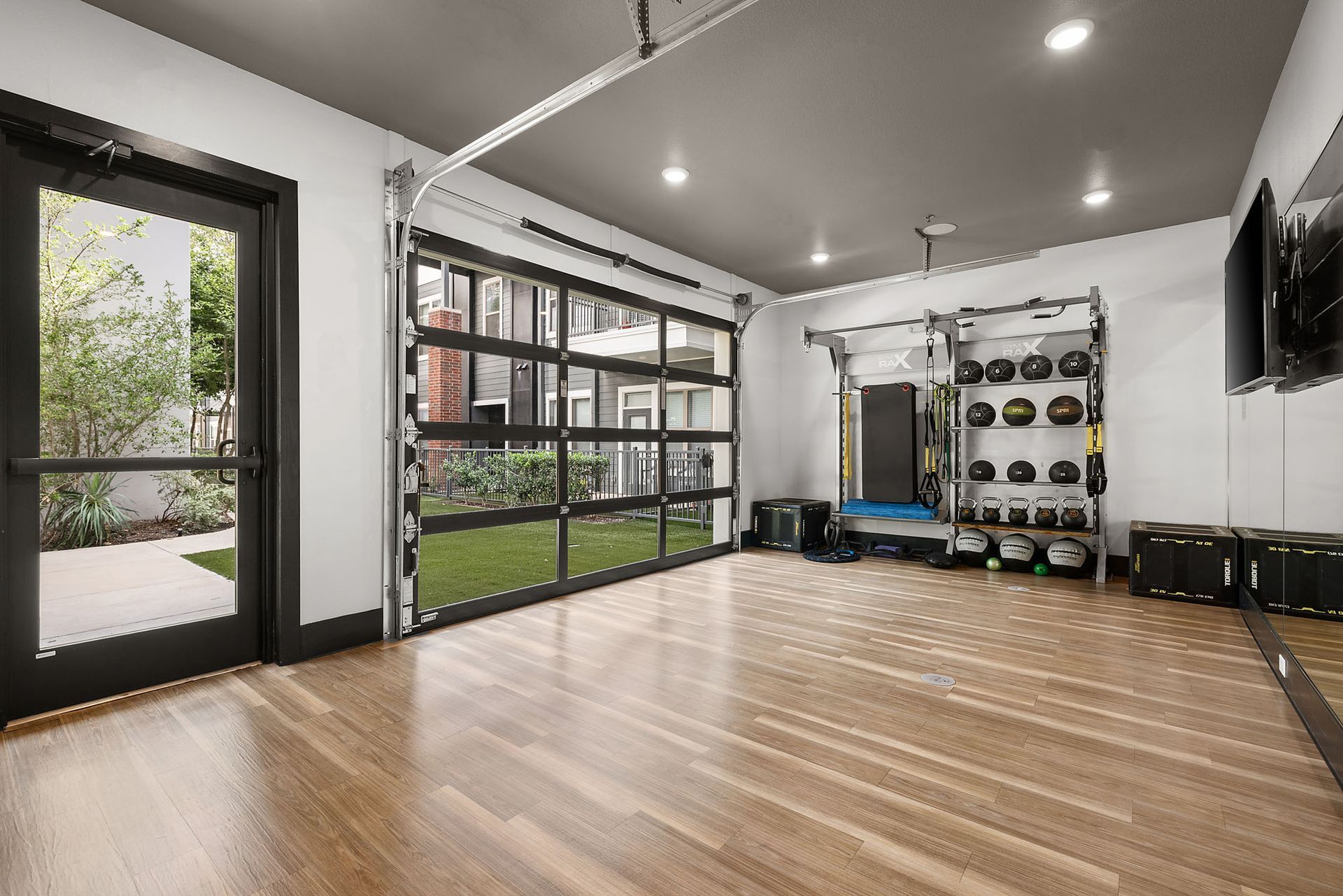 Modern fitness studio with wood floor, wall mirrors, equipment rack, and large windows overlooking greenery at Two99 Monroe.