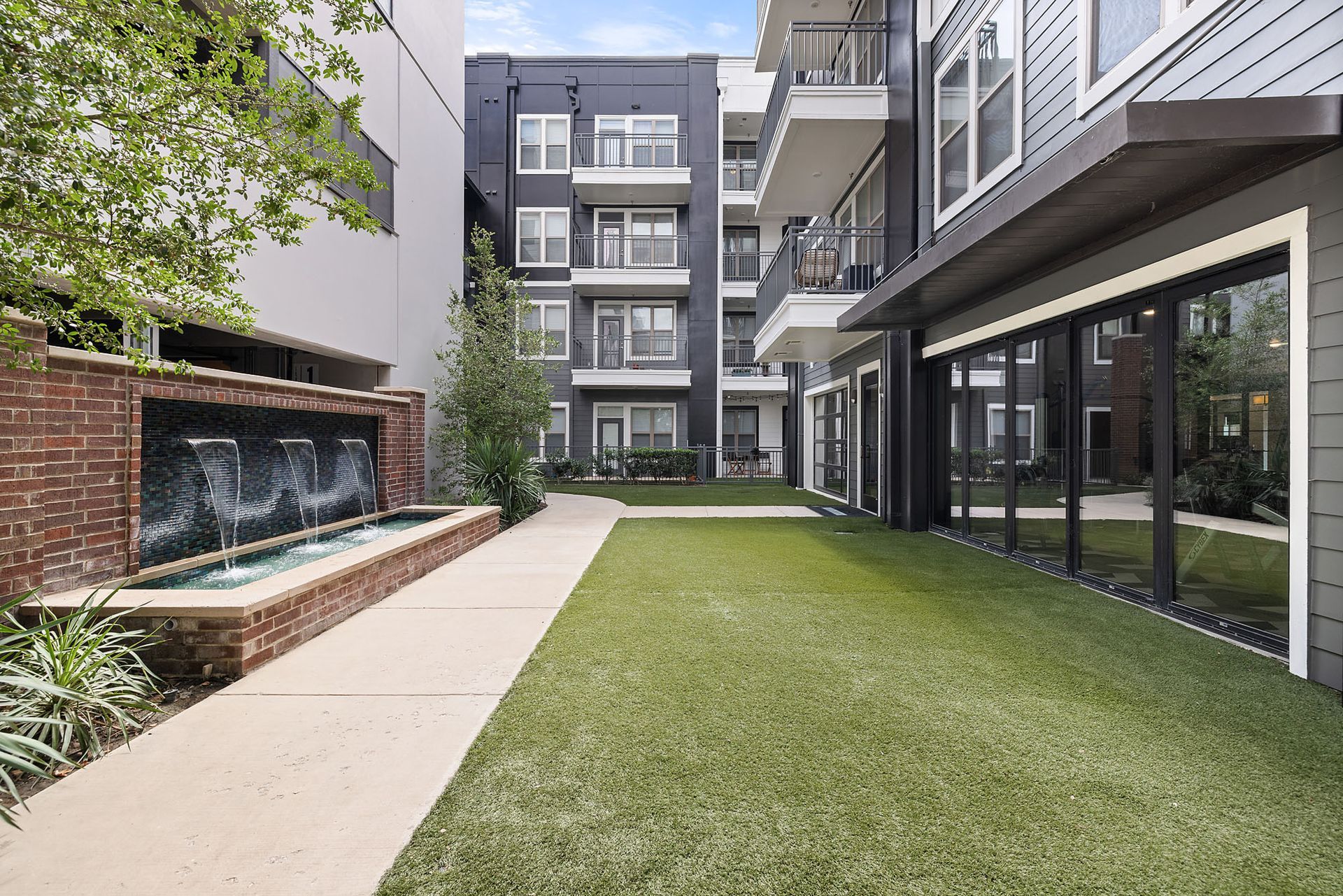 Modern apartment courtyard with green lawn, brick fountain wall, and glass balconies at Two99 Monroe.
