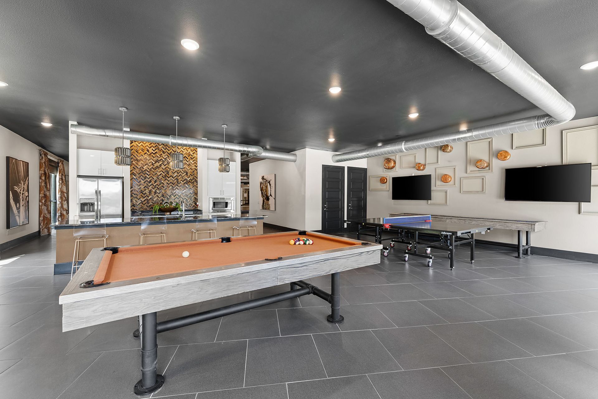Modern game room with a pool table, ping-pong table, and wall-mounted TVs at Two99 Monroe