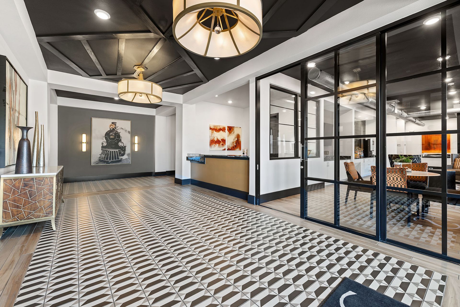 Modern office lobby with patterned tile floor, glass-walled meeting rooms, and pendant lights at Two99 Monroe.