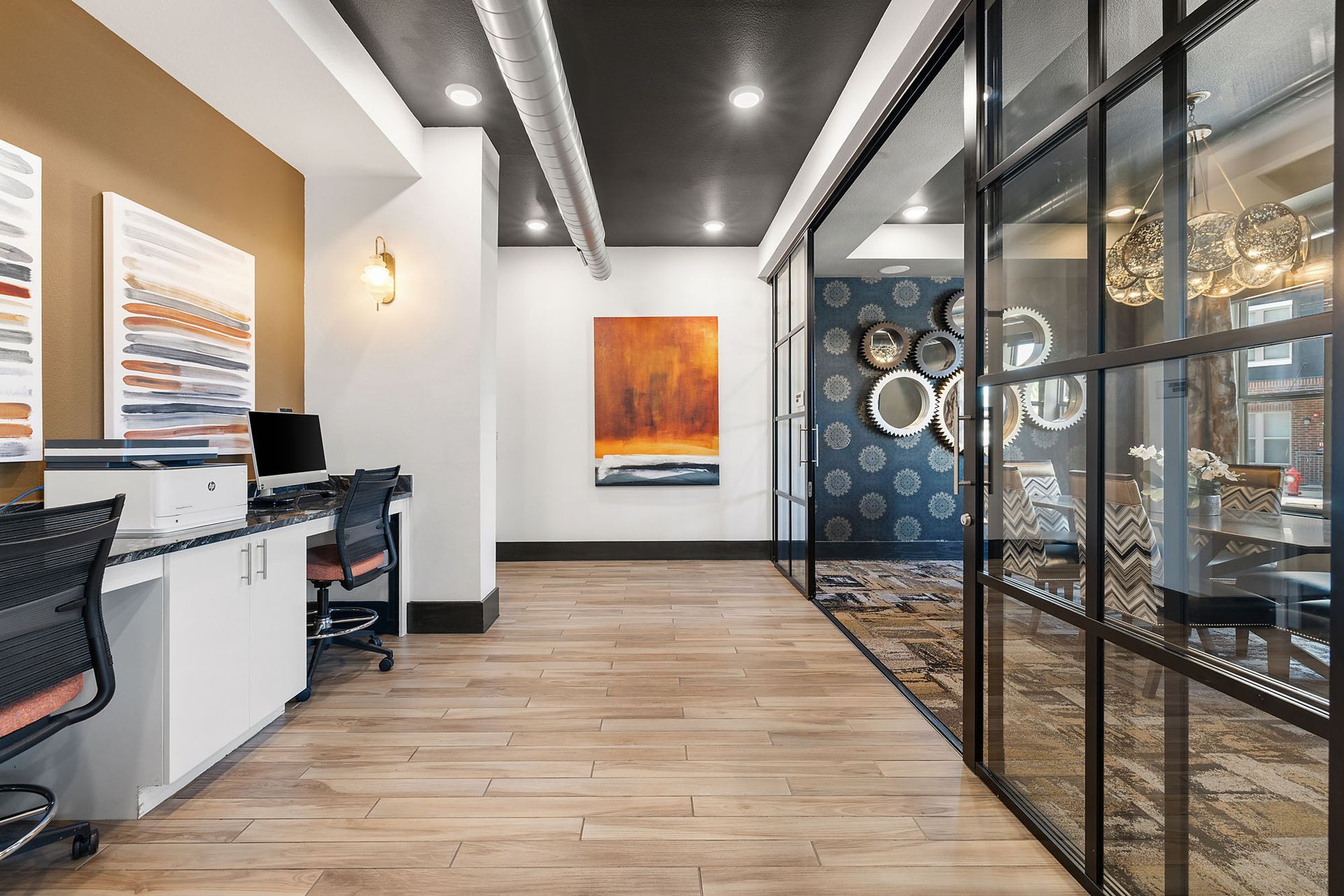 Modern office hallway with wood floors, glass-walled rooms, and colorful wall art at Two99 Monroe