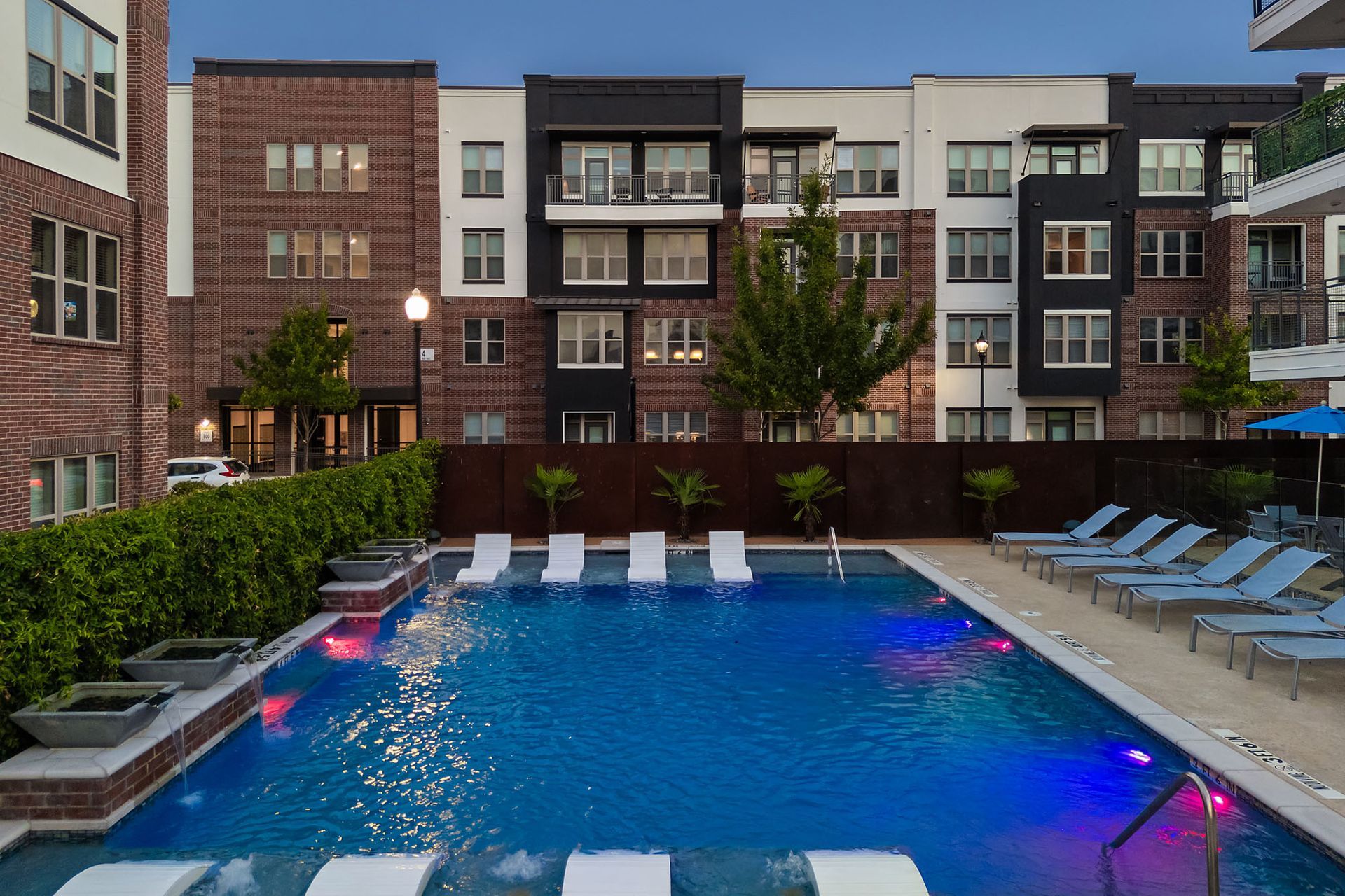 Apartment courtyard pool at dusk with blue water, lounge chairs, and lit buildings surrounding it at Two99 Monroe.