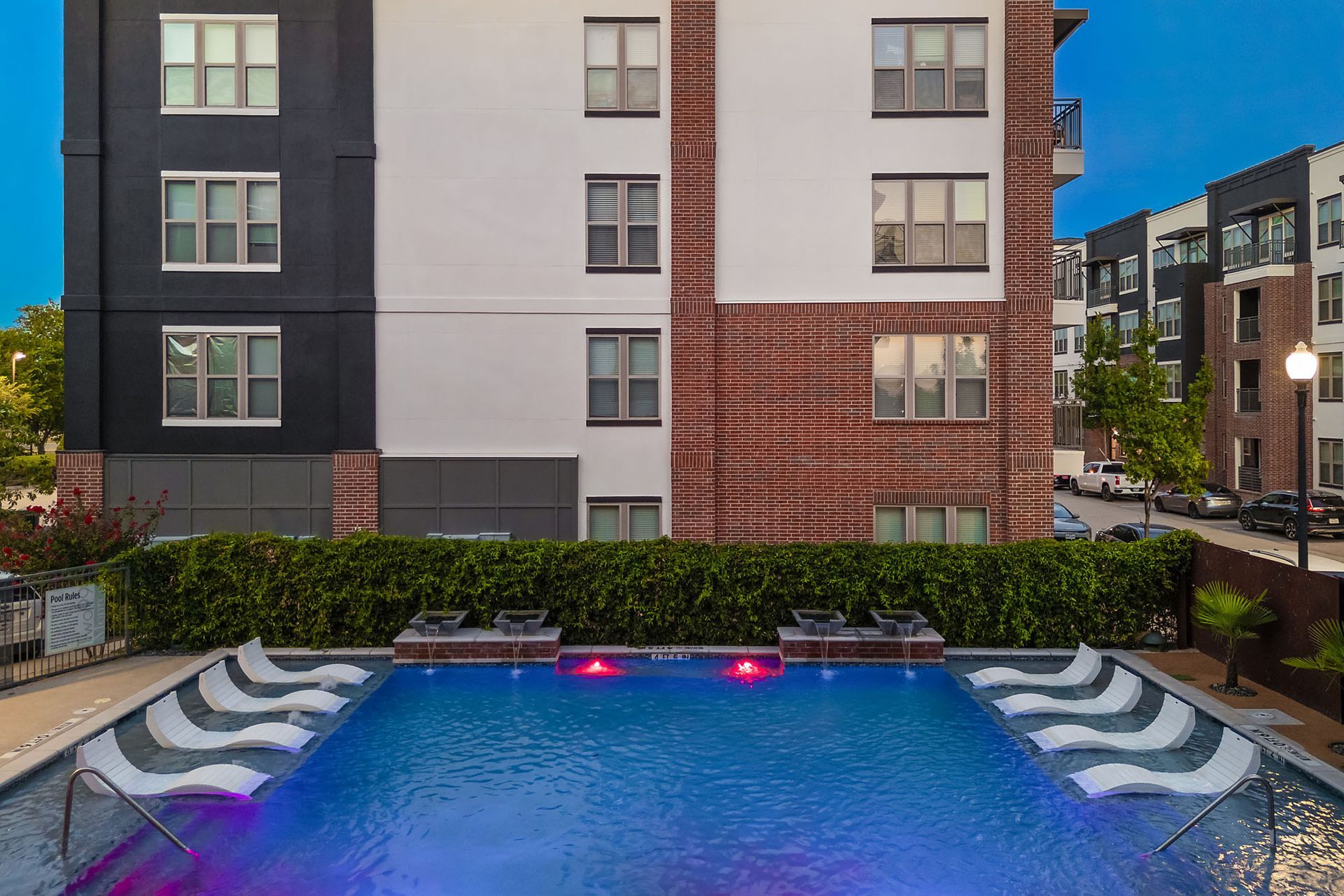 Apartment courtyard pool at dusk with blue water, red lights, and surrounding buildings at Two99 Monroe.