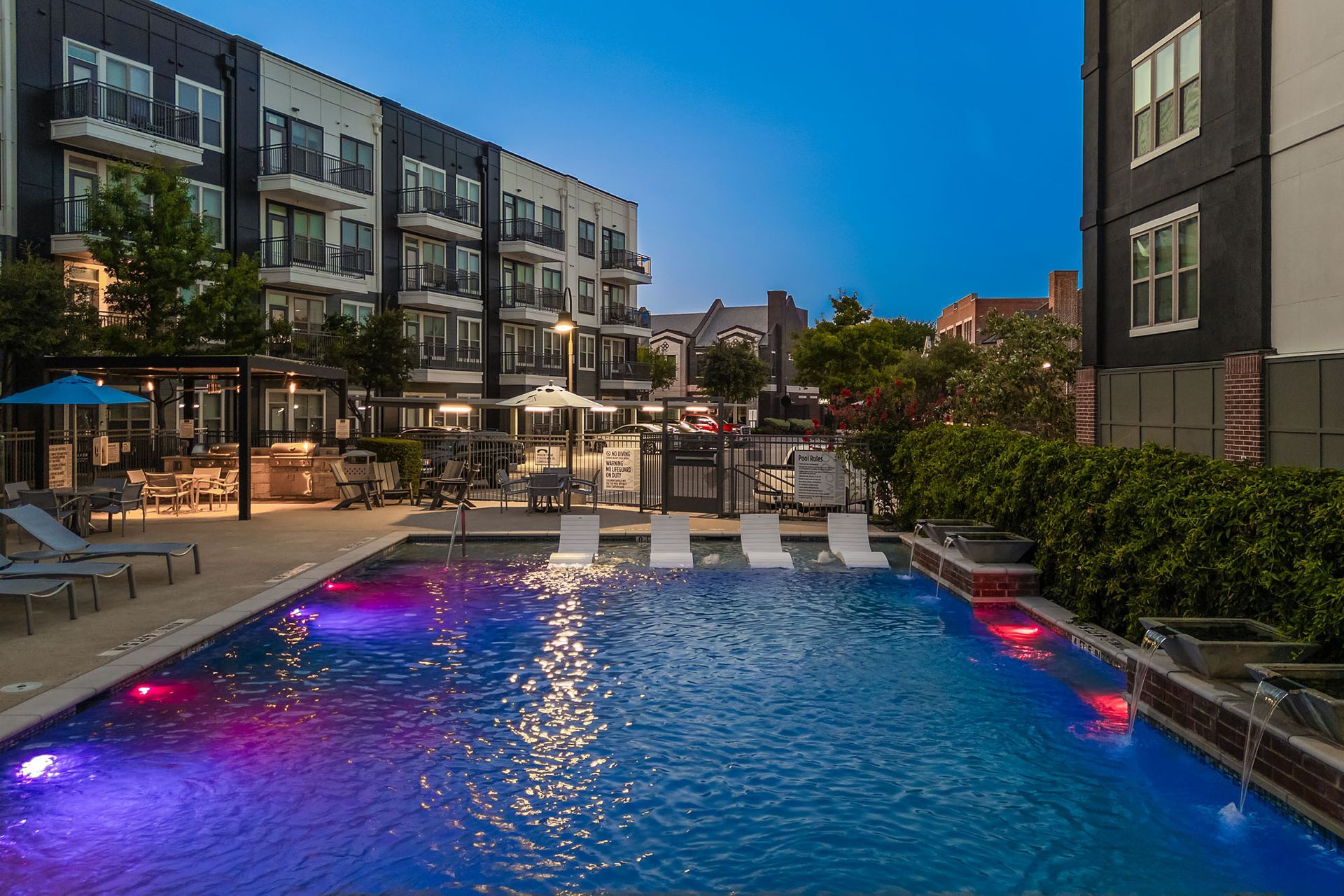 Lit apartment pool at dusk with blue water and pink underwater lights, surrounded by modern buildings at Two99 Monroe.
