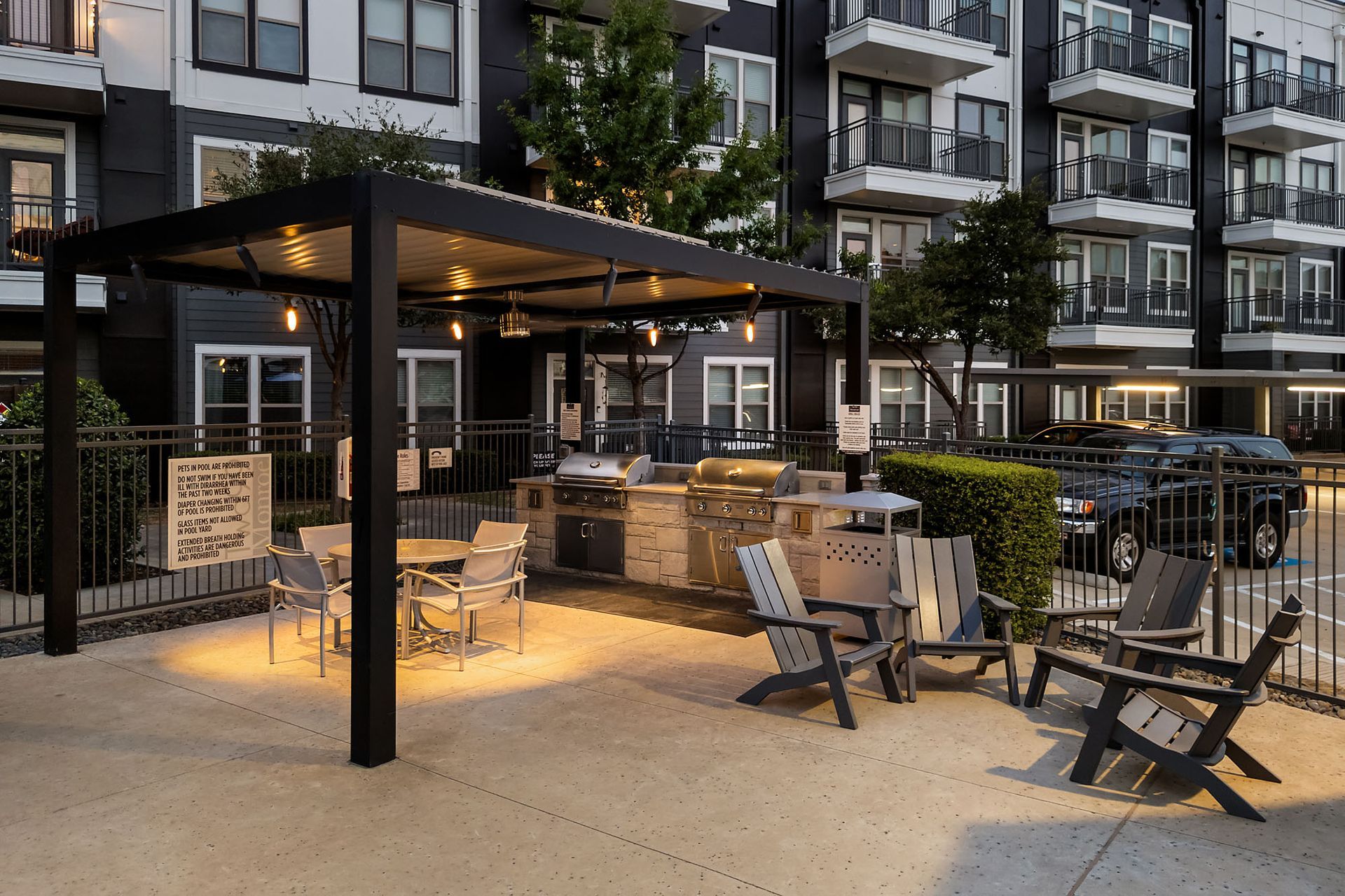 Modern apartment courtyard with a lit outdoor lounge, fire pit, and seating area at dusk at Two99 Monroe.