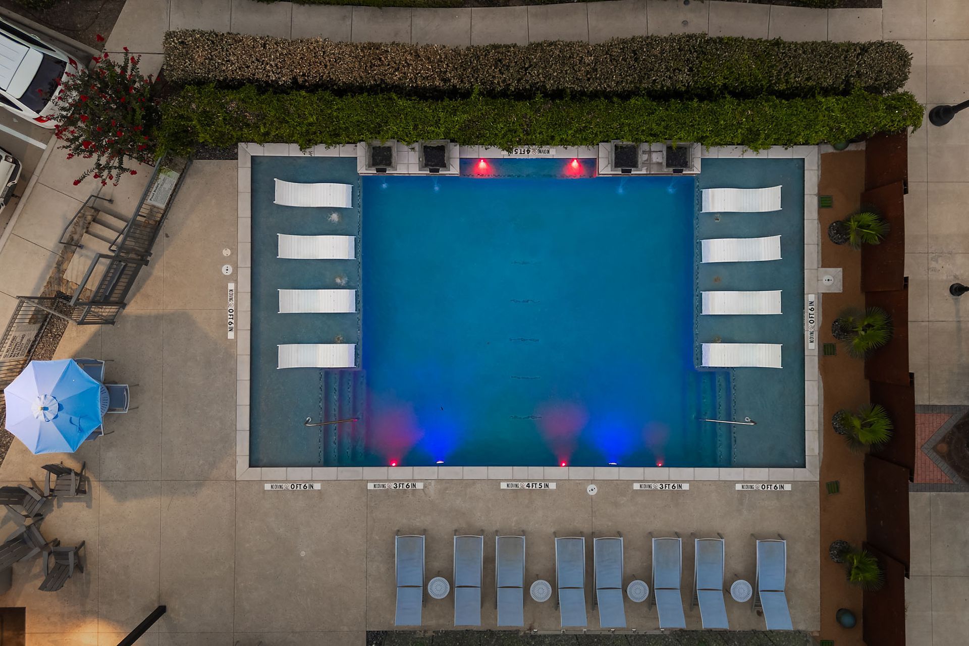 Overhead view of a lit outdoor swimming pool with lounge chairs around it at dusk at Two99 Monroe.