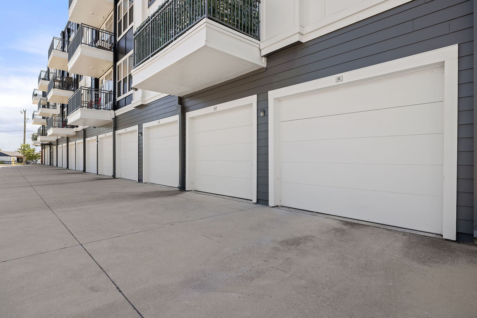 Row of white garage doors beside gray apartment balconies along a concrete driveway at Two99 Monroe.