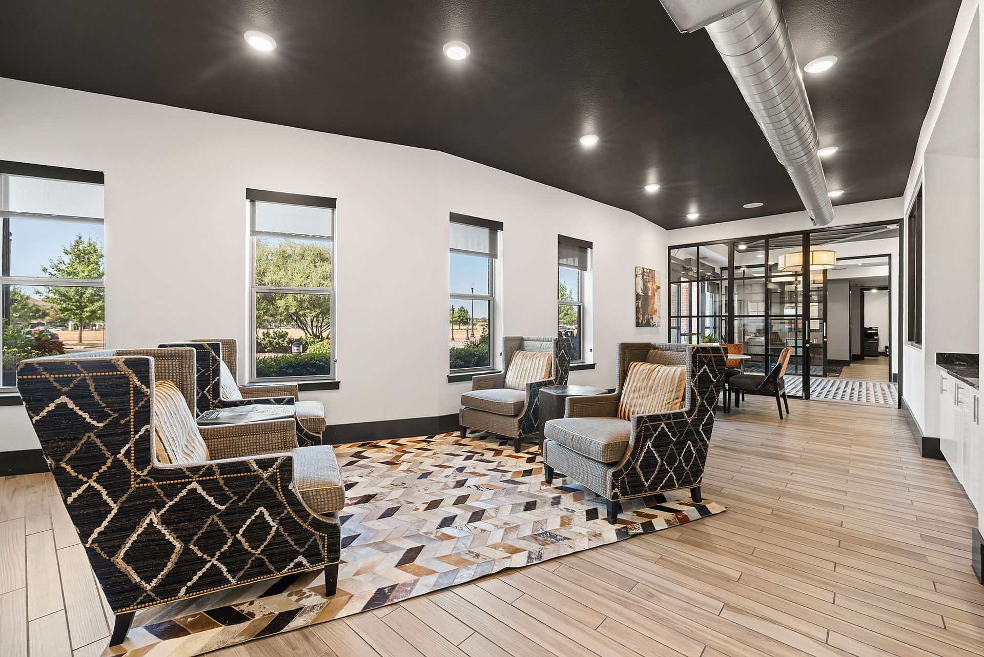 Modern lounge with patterned chairs, large windows, and a white curved wall under dark ceiling lights at Two99 Monroe