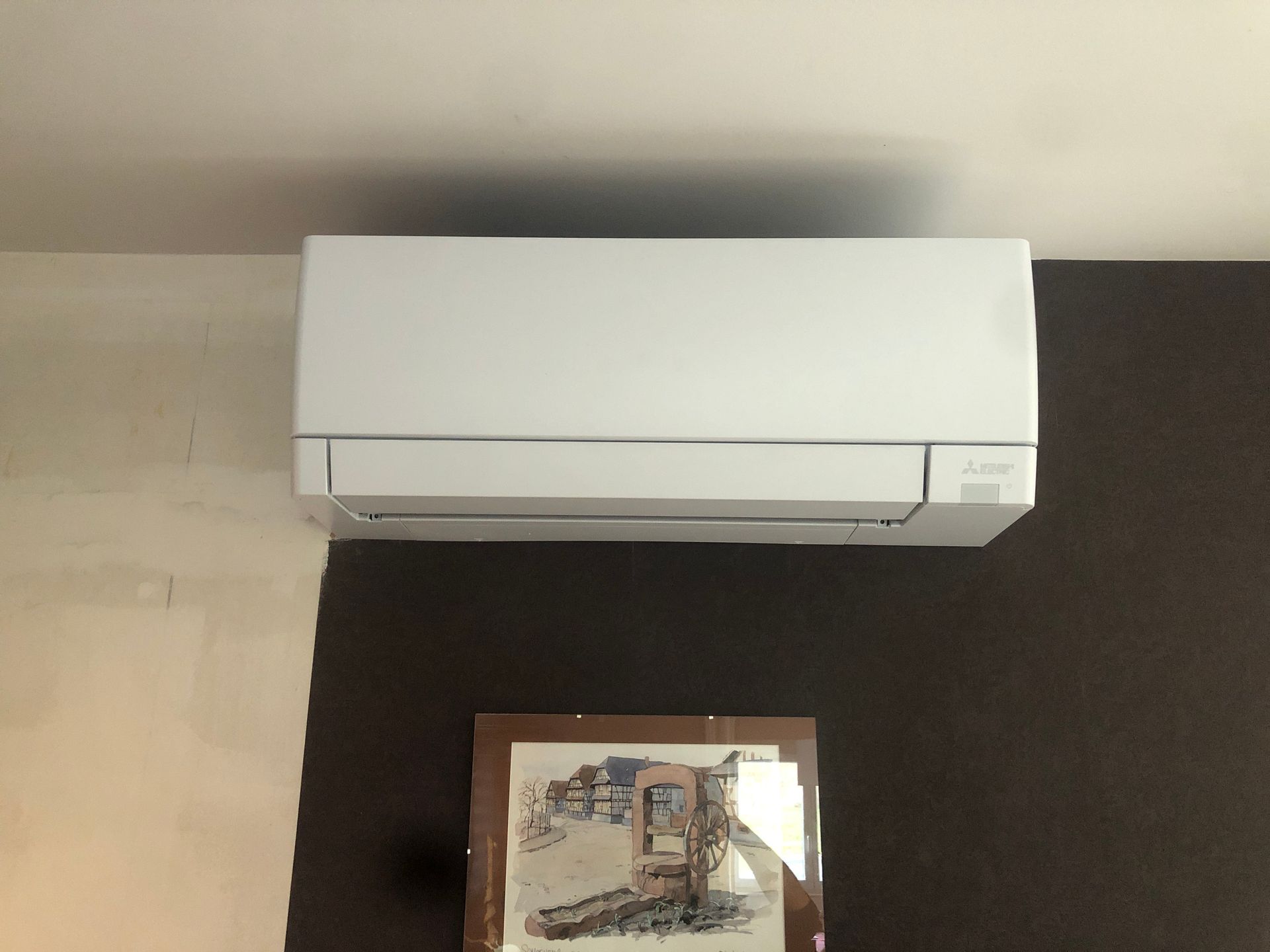 Climatiseur blanc mural au-dessus d'un tableau encadré sur un mur beige