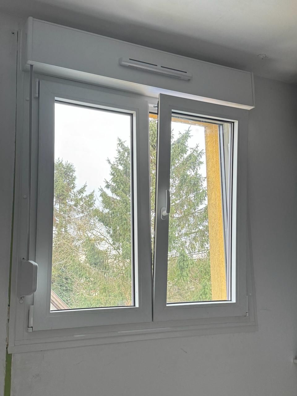 Fenêtre intérieure blanche donnant sur des arbres visibles à l'extérieur et un étroit rideau jaune sur le côté droit.