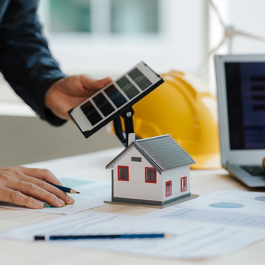 Une personne tient un panneau solaire au-dessus d'une maison modèle