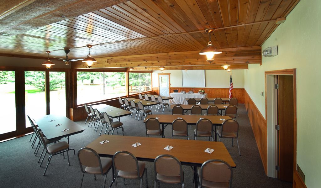 Empty conference room with wooden ceiling, tables, chairs, and large windows overlooking greenery