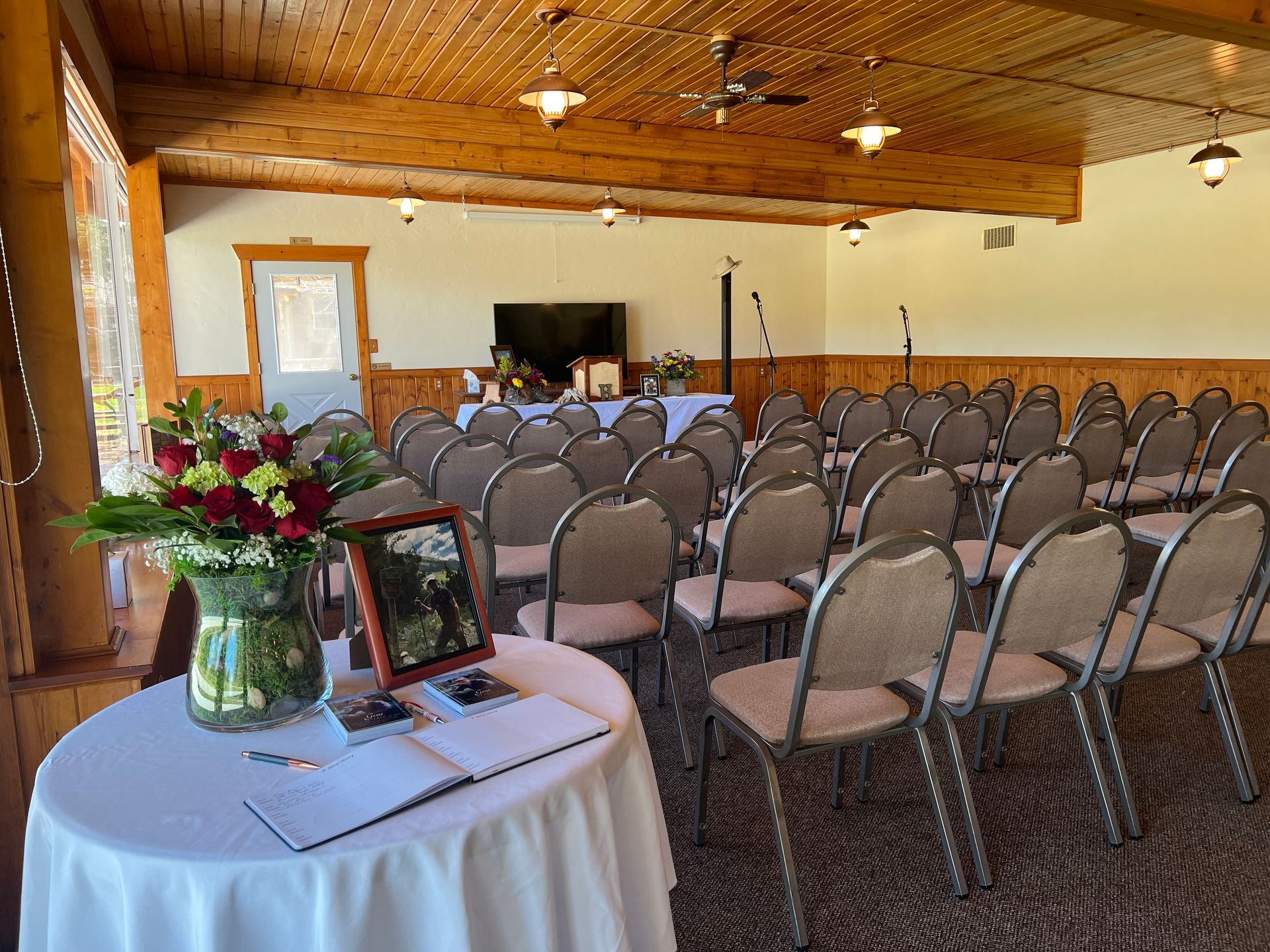 Banquet hall with rows of chairs facing a small stage, and a decorated table with flowers in the foreground