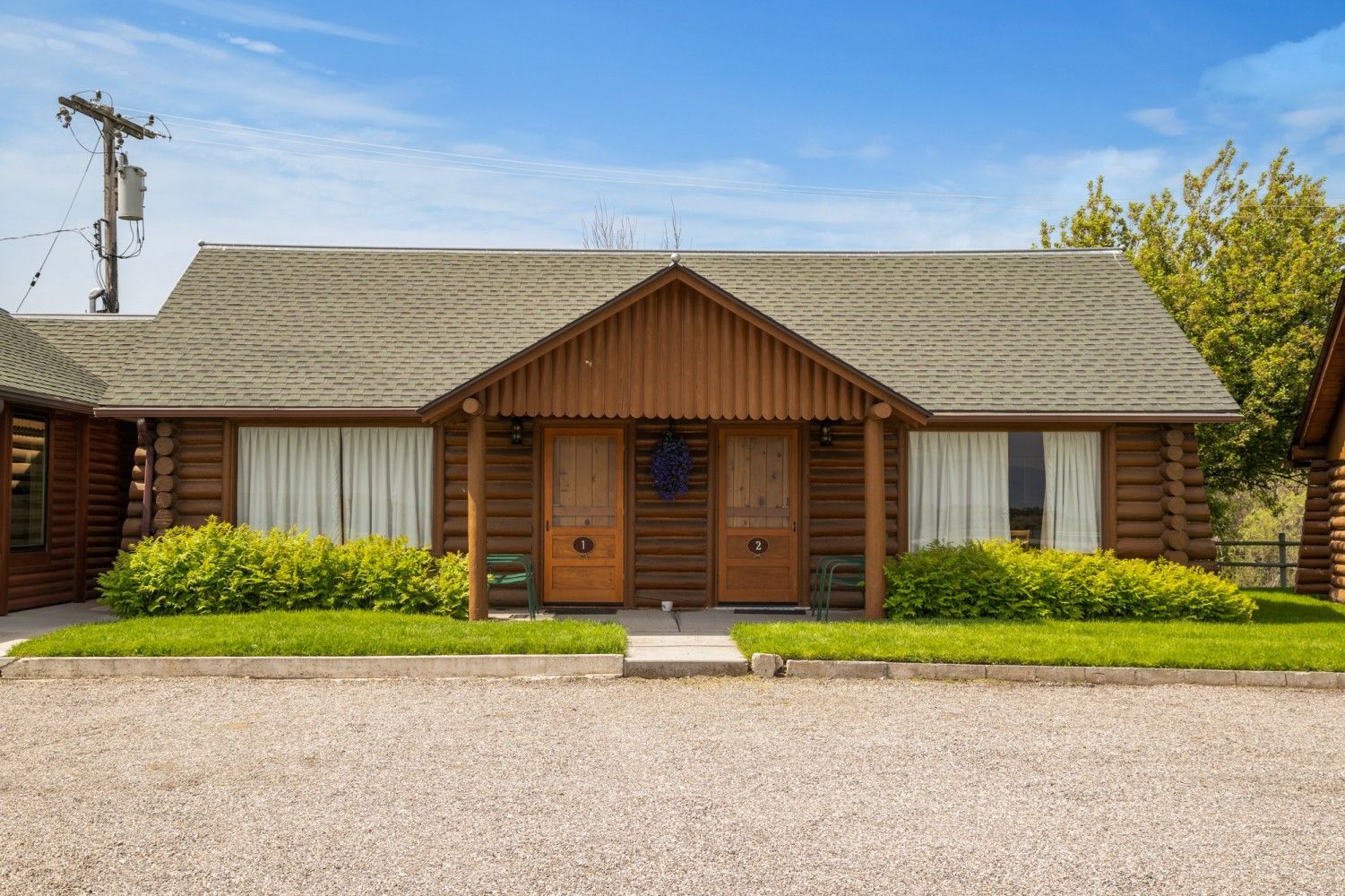 Wooden cabin-style house with a central entrance, shingled roof, and trimmed hedges in front.