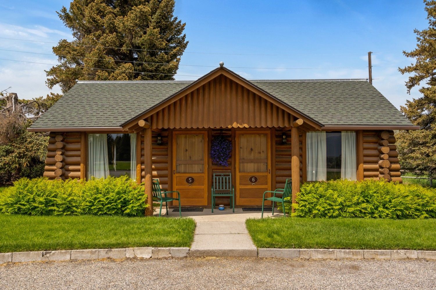 Log cabin-style house with a covered porch, green hedges, and a clear blue sky