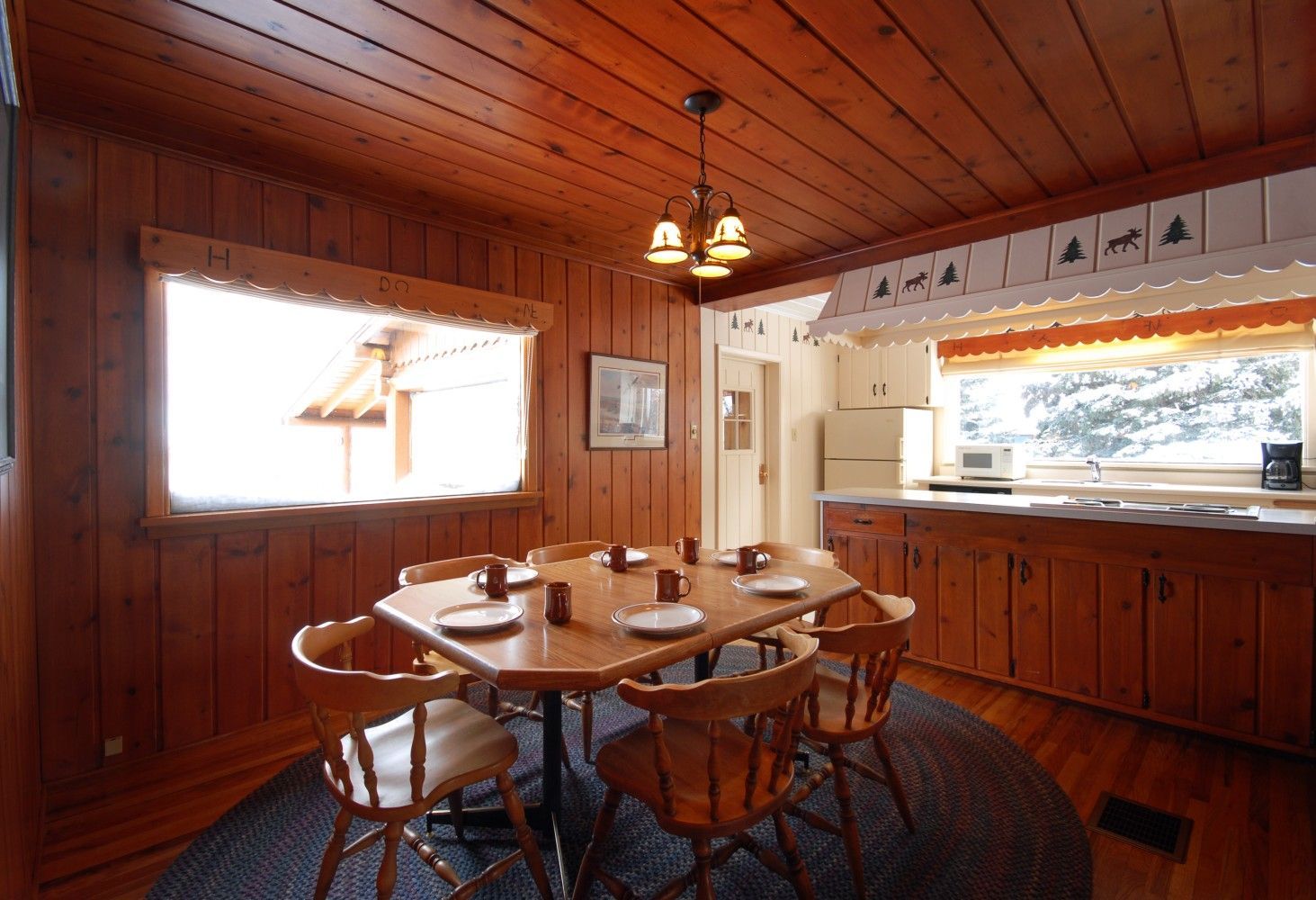 Wood-paneled dining room with a round table, wooden chairs, and large windows letting in daylight
