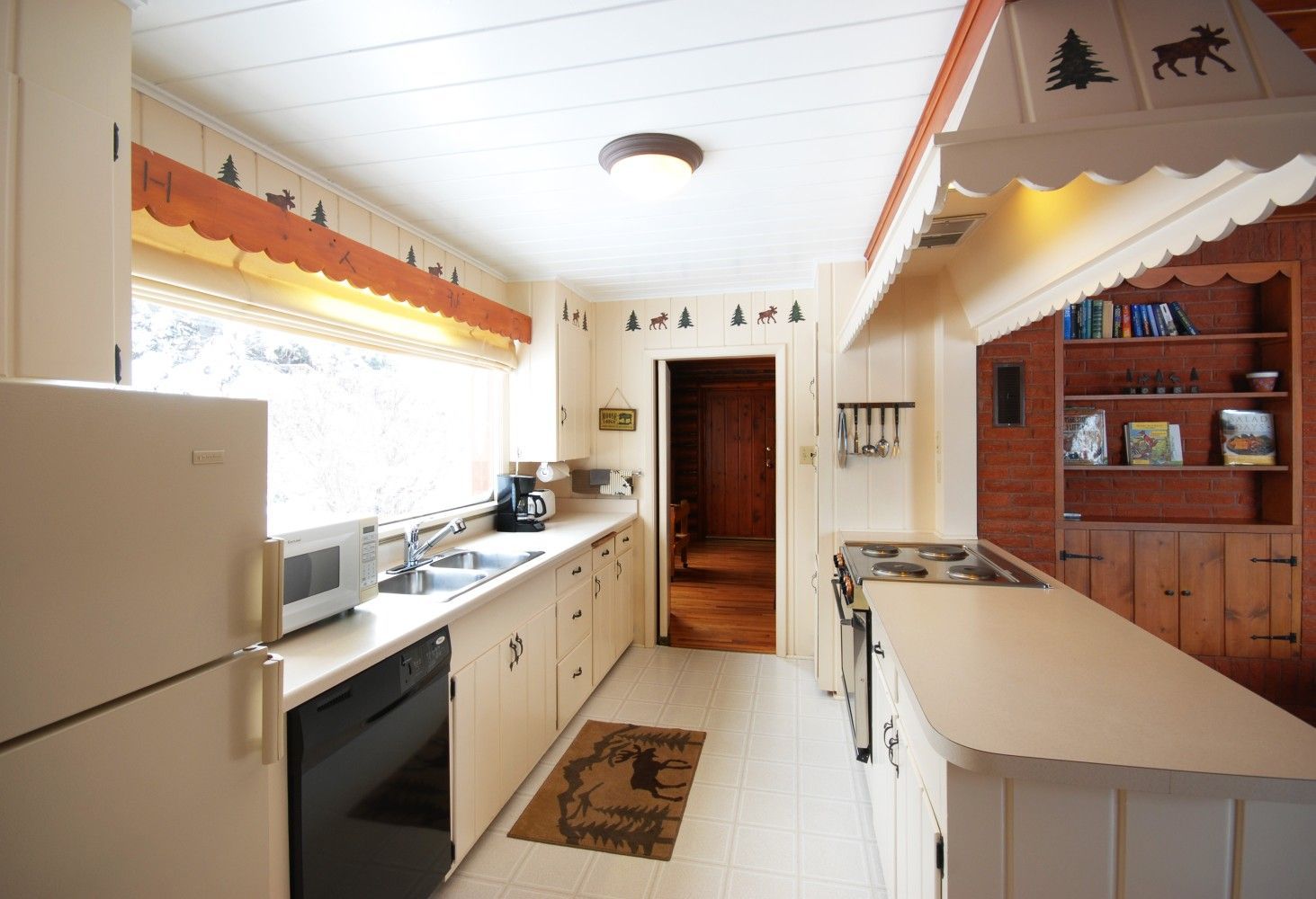 Bright, narrow kitchen with white cabinets, long counter, island, and wood hutch in a rustic cabin style.