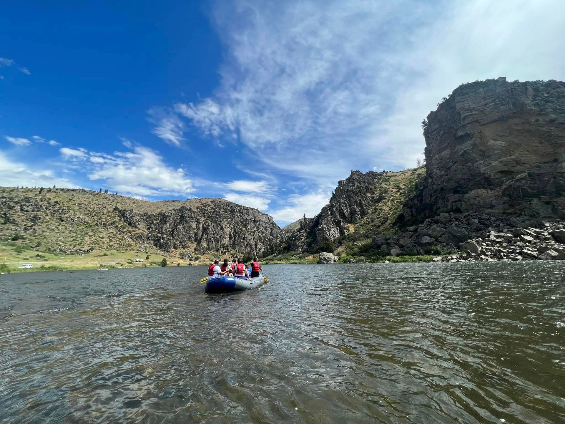 People rafting on a river between rocky cliffs under a blue, cloudy sky