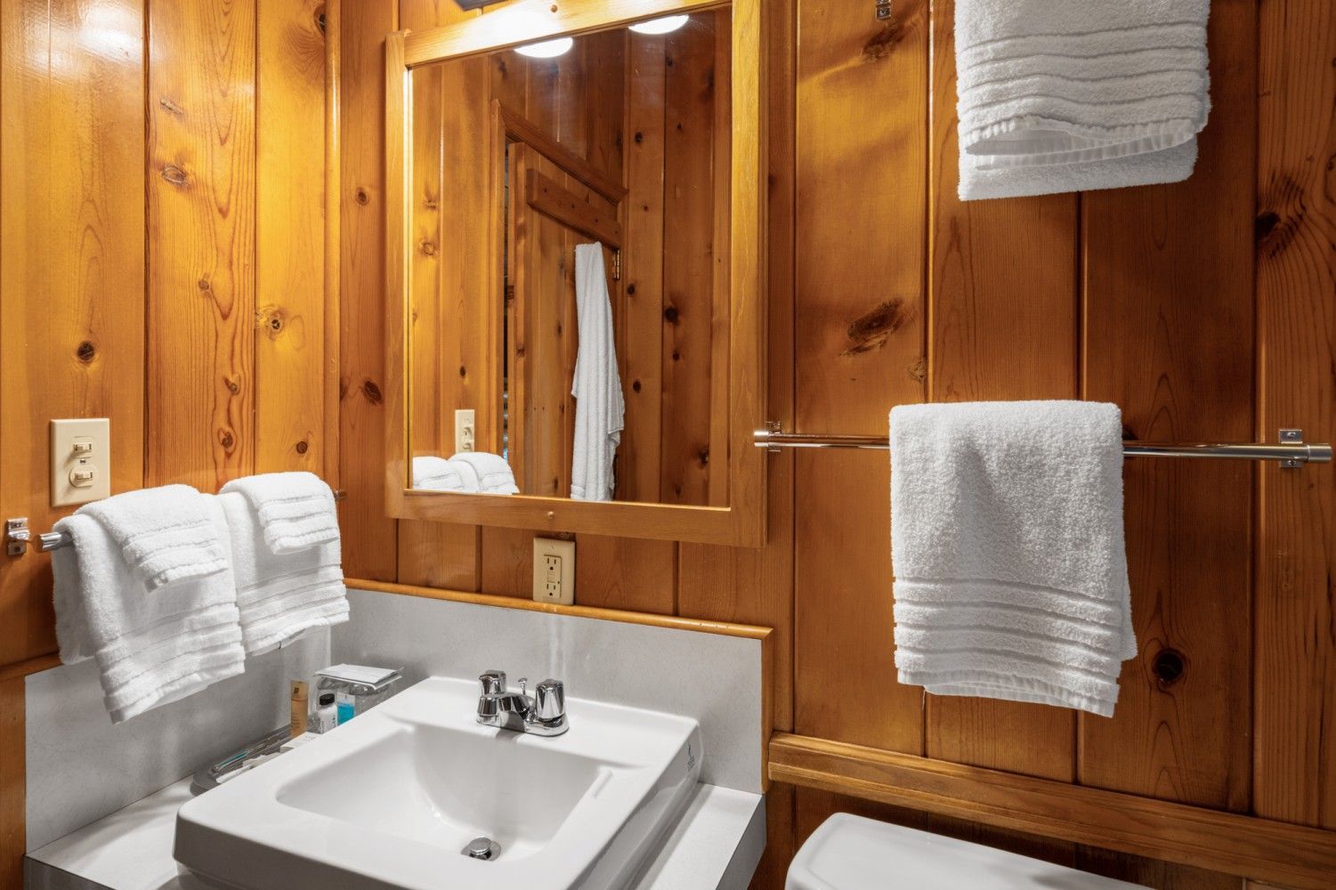 Wood-paneled bathroom with a white sink, mirror, and neatly hung towels