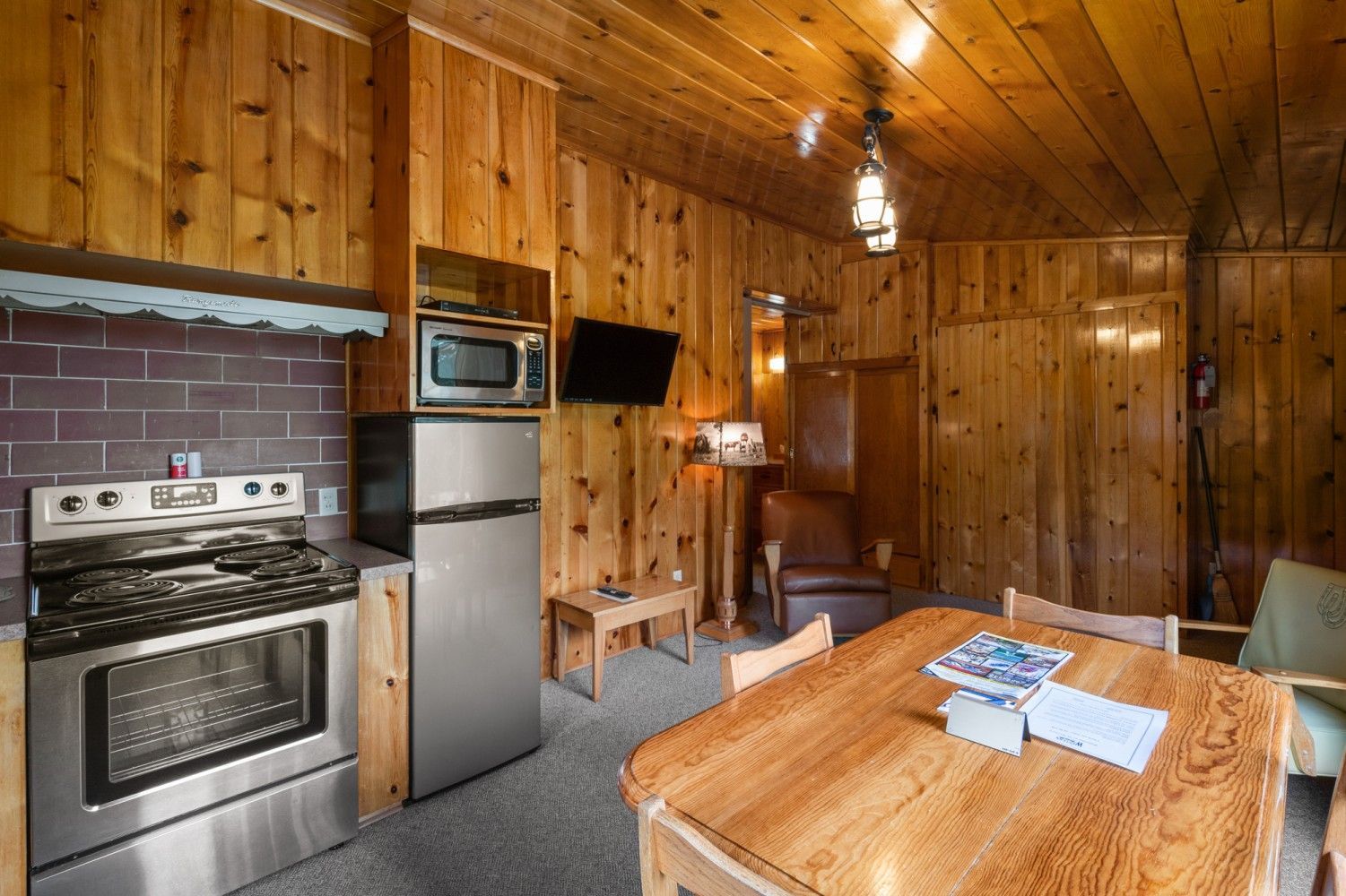 Wood-paneled cabin kitchen and dining area with stove, refrigerator, microwave, and wooden table