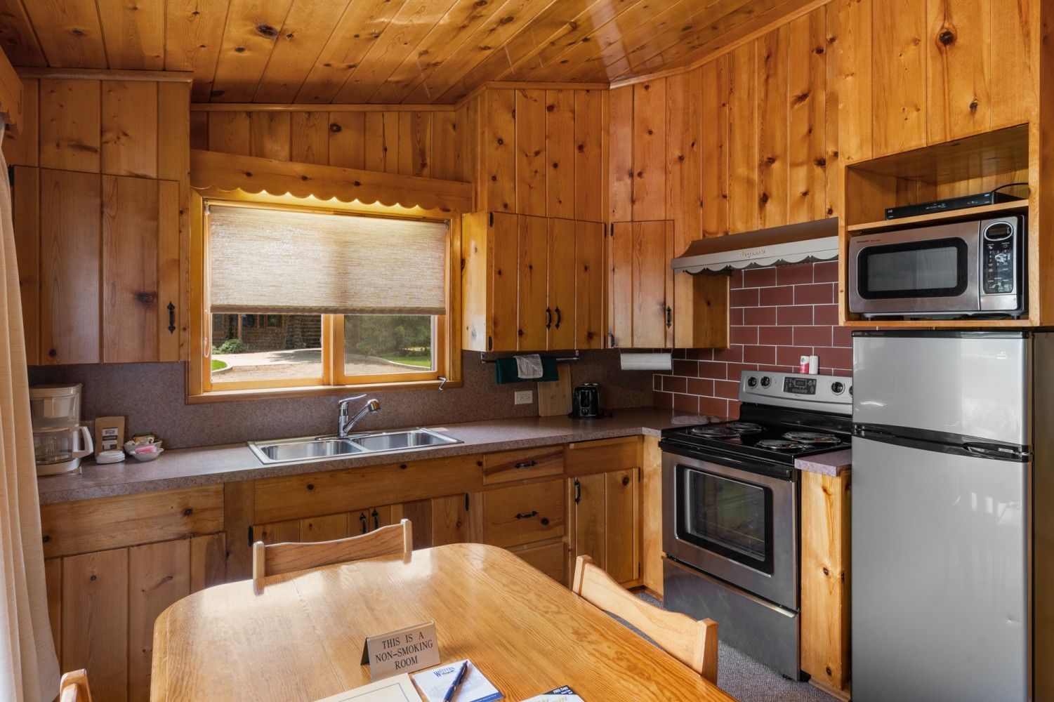 Wood-paneled kitchen with wooden table, window sink, stove, microwave, and refrigerator