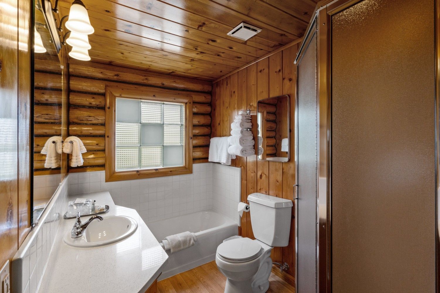 Wood-paneled bathroom with sink, toilet, shower, window, and frosted glass door