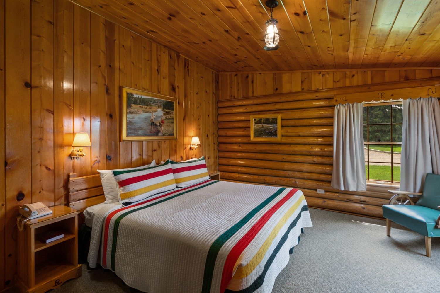 Wood-paneled bedroom with a striped bedspread, window with curtains, and a teal chair