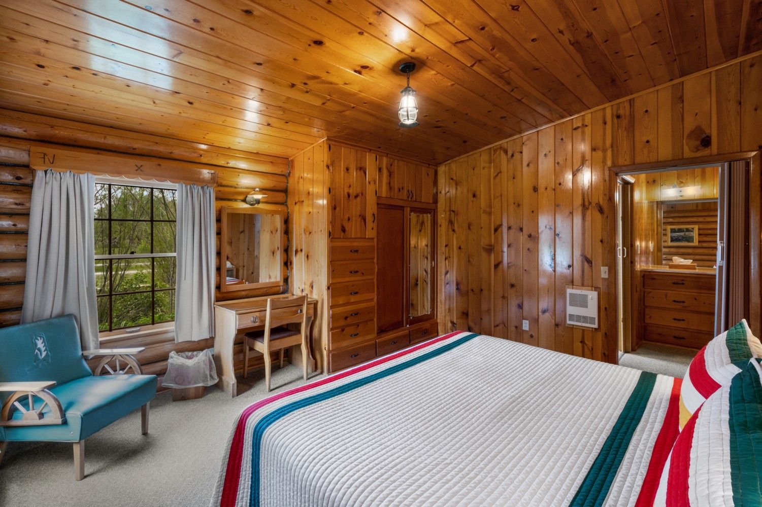 Wood-paneled bedroom with a bed, window seating, desk, and warm ceiling light