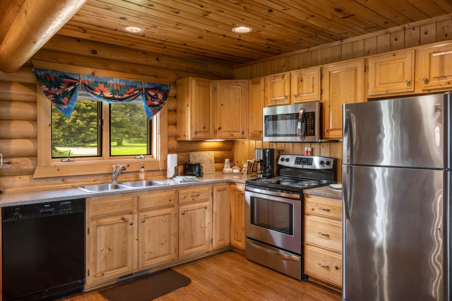 Wood-paneled kitchen with wooden cabinets, stainless steel appliances, and a window over the sink.